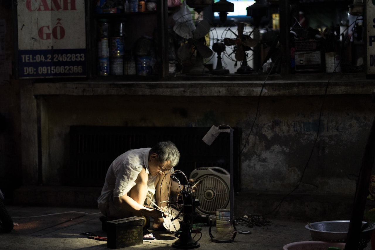 A man fixing an old fan outside a shop in Hanoi in the evening
