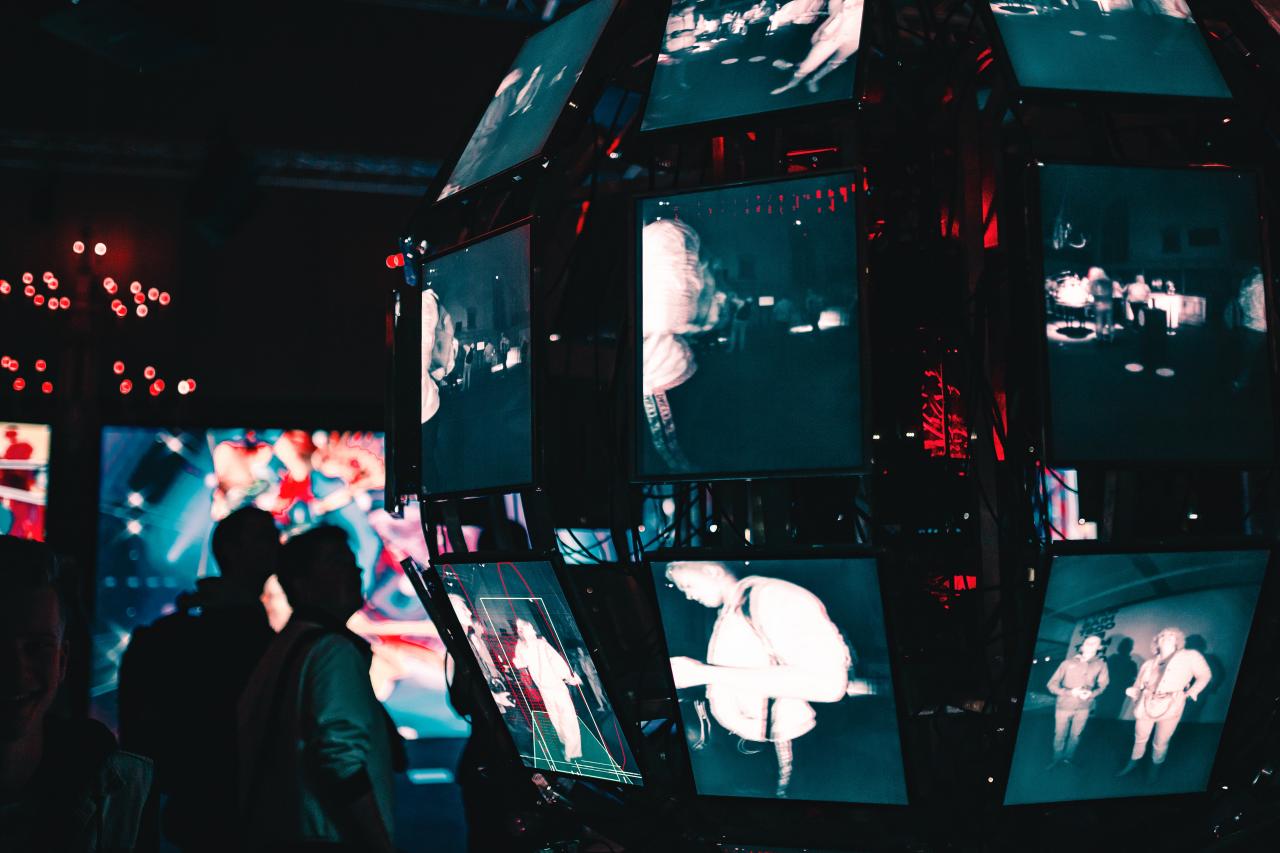 Two men stare at a technological art exhibit with many screens